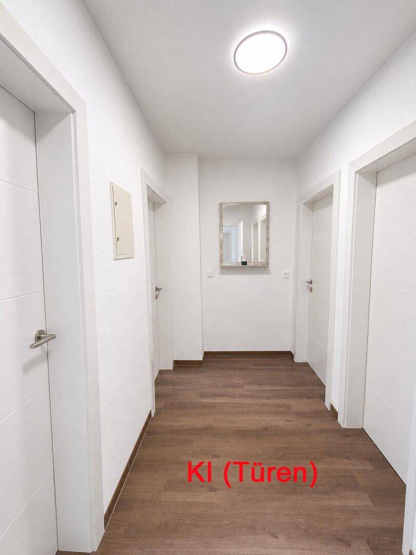 Moderner Flur mit hellem Holzboden, weißen Wänden und minimalistischen weißen Türen.