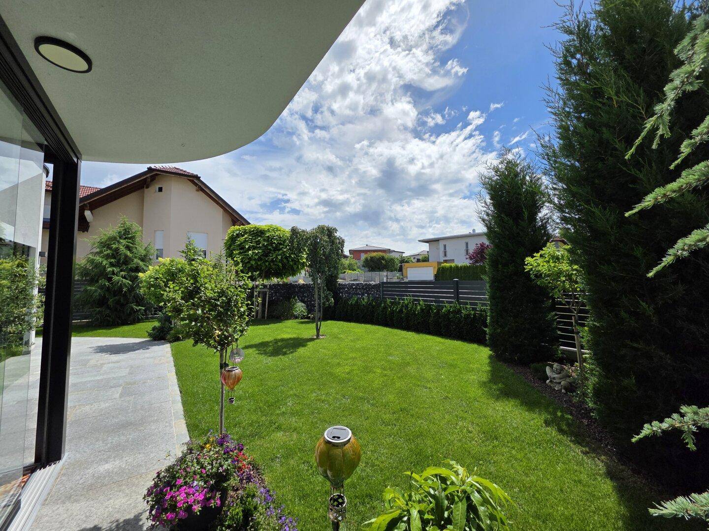 Gepflegter Gartenbereich mit Rasenfläche und Zierbäumen, umgeben von einer modernen Wohnbebauung.