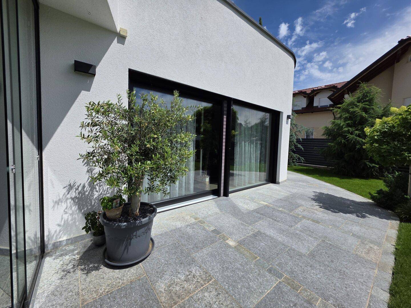 Geräumige Steinterrasse mit großformatigen Fliesen und Zugang zum Haus durch breite Glasschiebetüren.