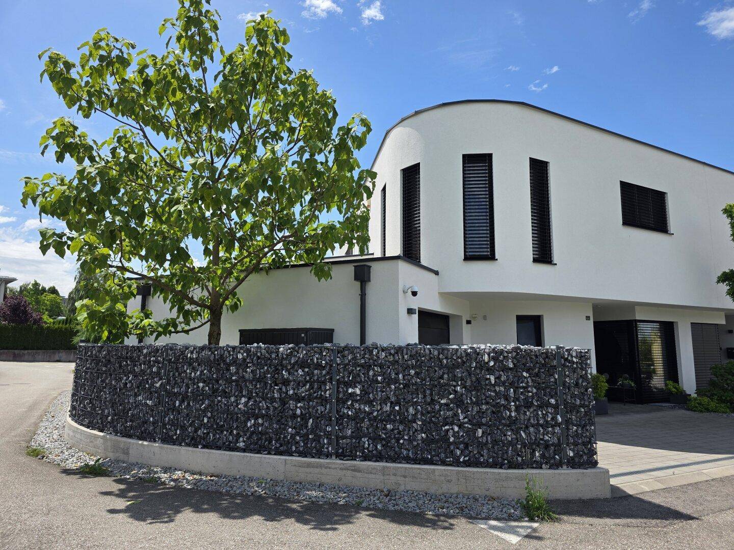 Modernes Wohnhaus mit geschwungener Architektur, weißen Fassaden und einer Gabionenmauer.