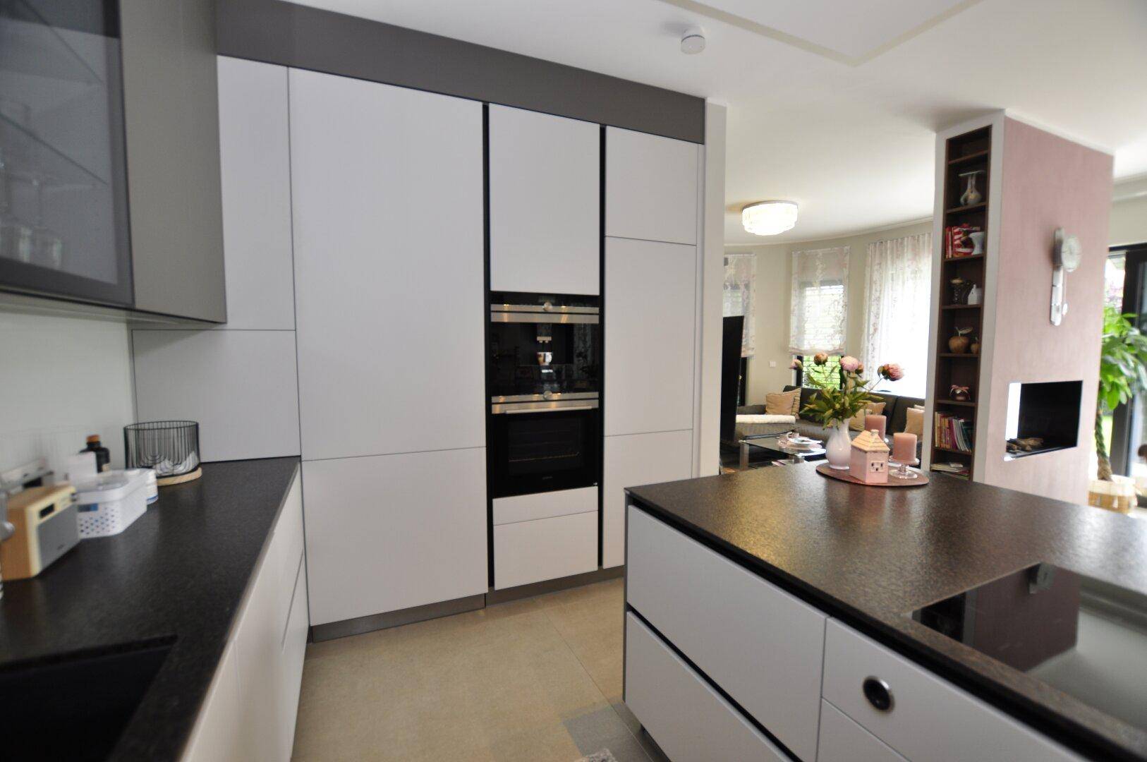 Hochwertige Einbauküche mit integriertem Backofen und Kaffeemaschine, dunklen Arbeitsplatten und viel Stauraum.