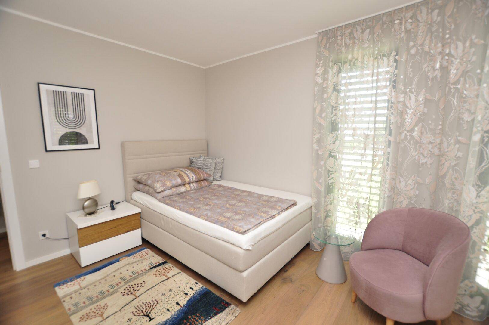 Helles Schlafzimmer mit Einzelbett, Holzboden und einem modernen Teppich sowie einem Sessel.