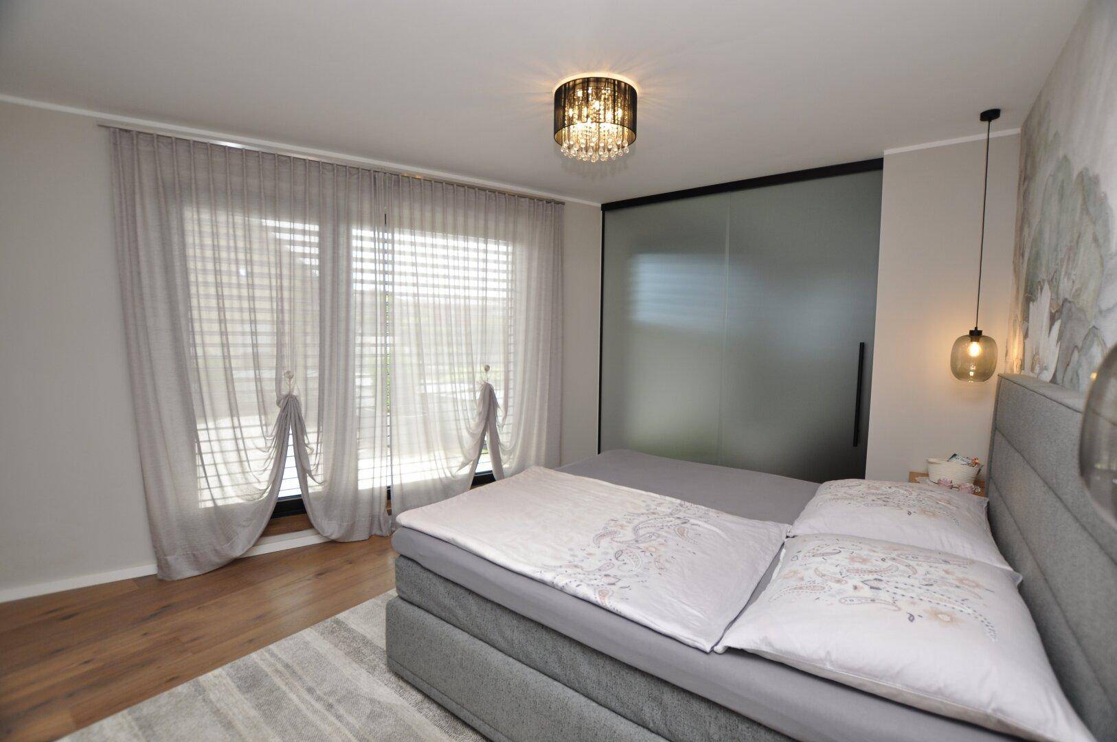 Modernes Schlafzimmer mit großem Bett, Holzboden und einer Schiebetür zu einem begehbaren Kleiderschrank.