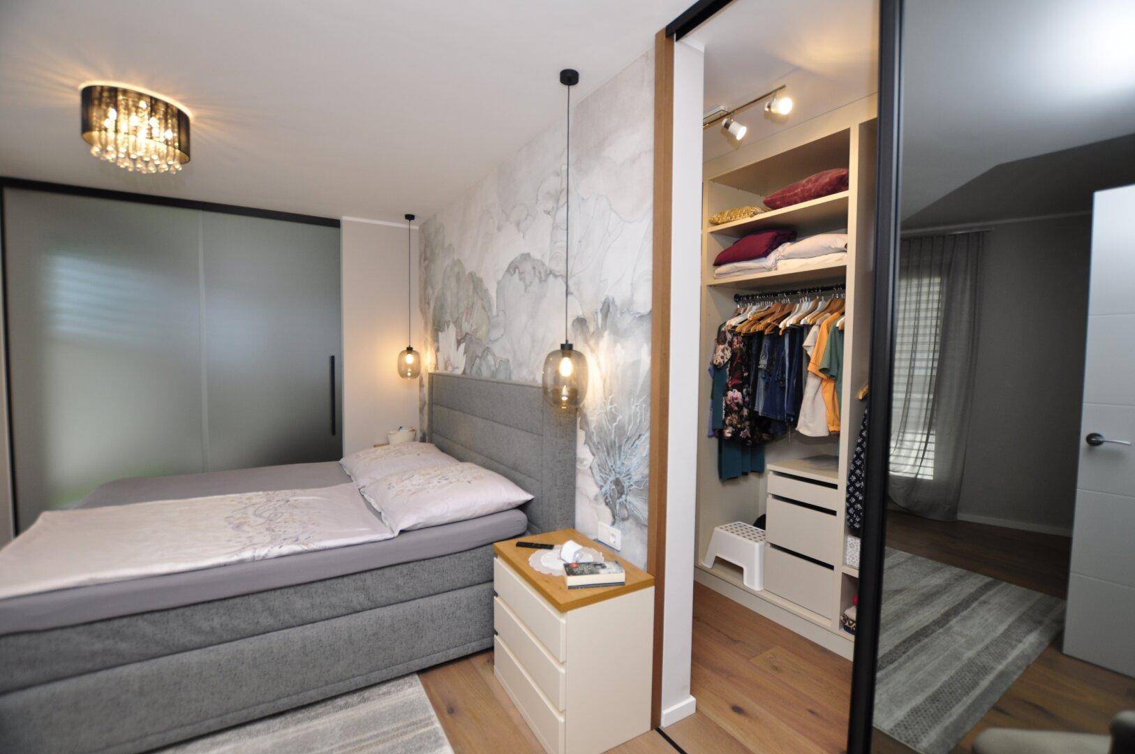 Schlafzimmer mit Doppelbett, Holzboden und offenem Zugang zu einem gut organisierten begehbaren Kleiderschrank.