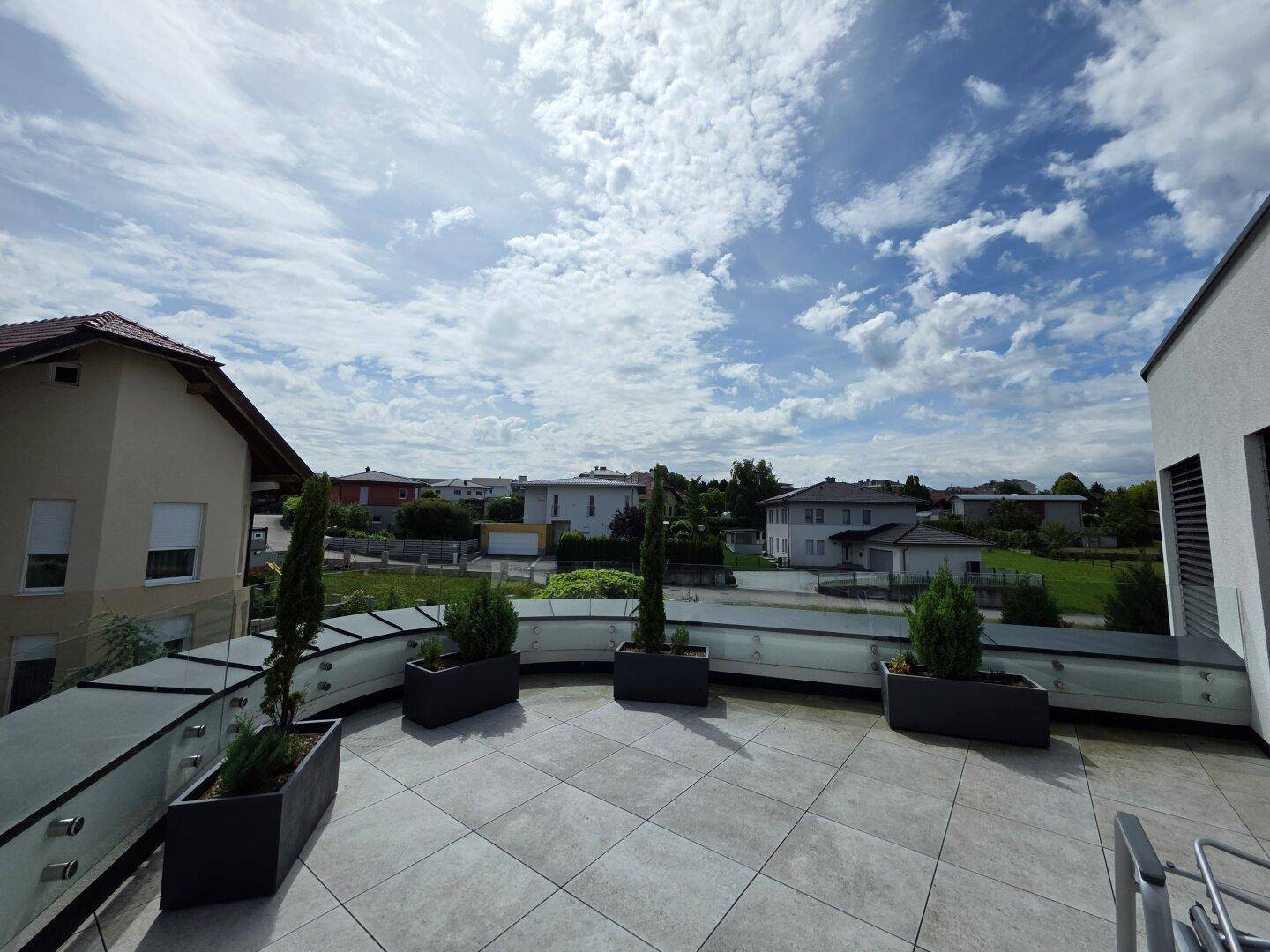 Geräumige Dachterrasse mit Fliesenboden, Glasbrüstung und weitem Blick über die Umgebung.
