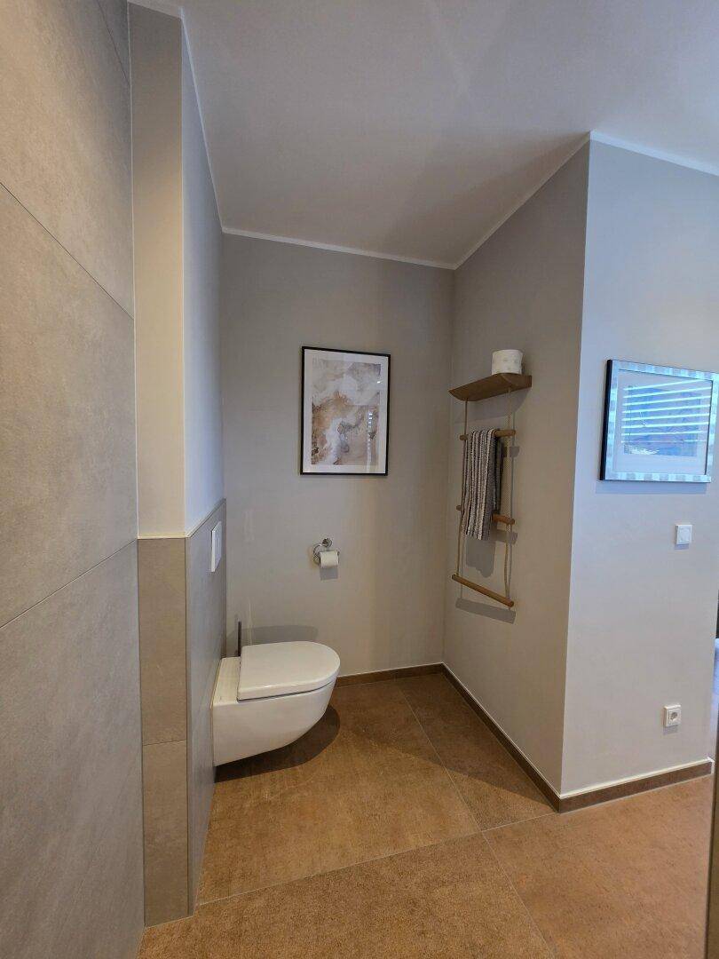 Modernes Gäste-WC mit wandhängender Toilette, stilvollen Fliesen und minimalistischer Dekoration.