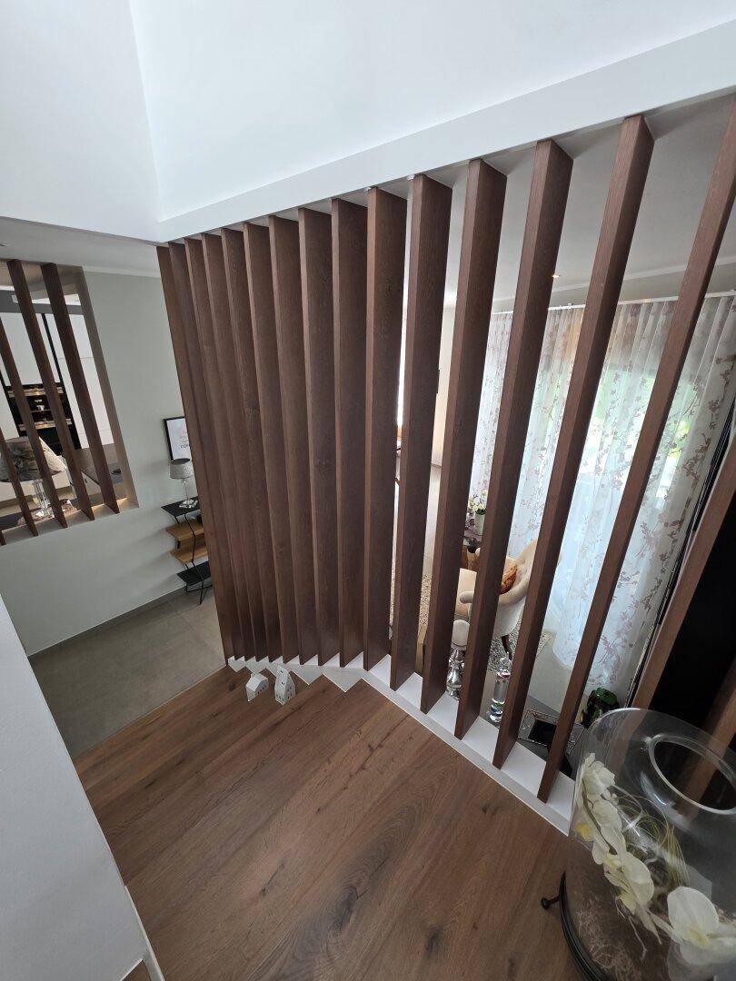 Blick von oben auf die moderne Holztreppe mit vertikalen Lamellen als Geländer.
