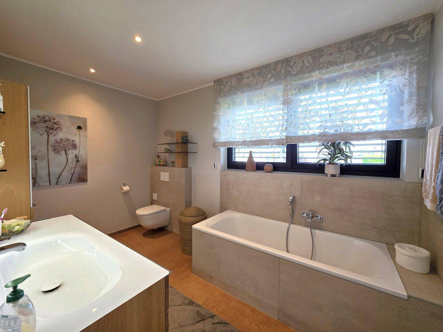 Modernes Badezimmer mit integrierter Badewanne, großem Waschtisch und Fenster für Tageslicht.