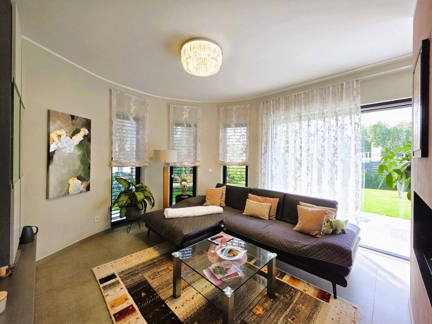 Gemütliches Wohnzimmer mit großem Ecksofa, modernem Teppich und Zugang zum Garten durch eine breite Glastür.