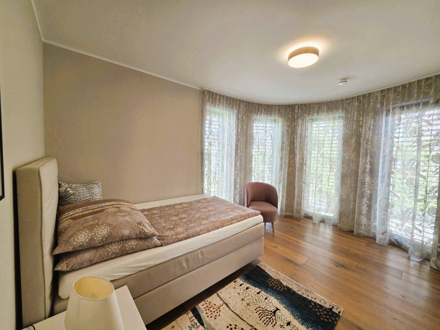 Schlafzimmer mit großem Fensterbereich, der viel Tageslicht hereinlässt, und einem bequemen Einzelbett.