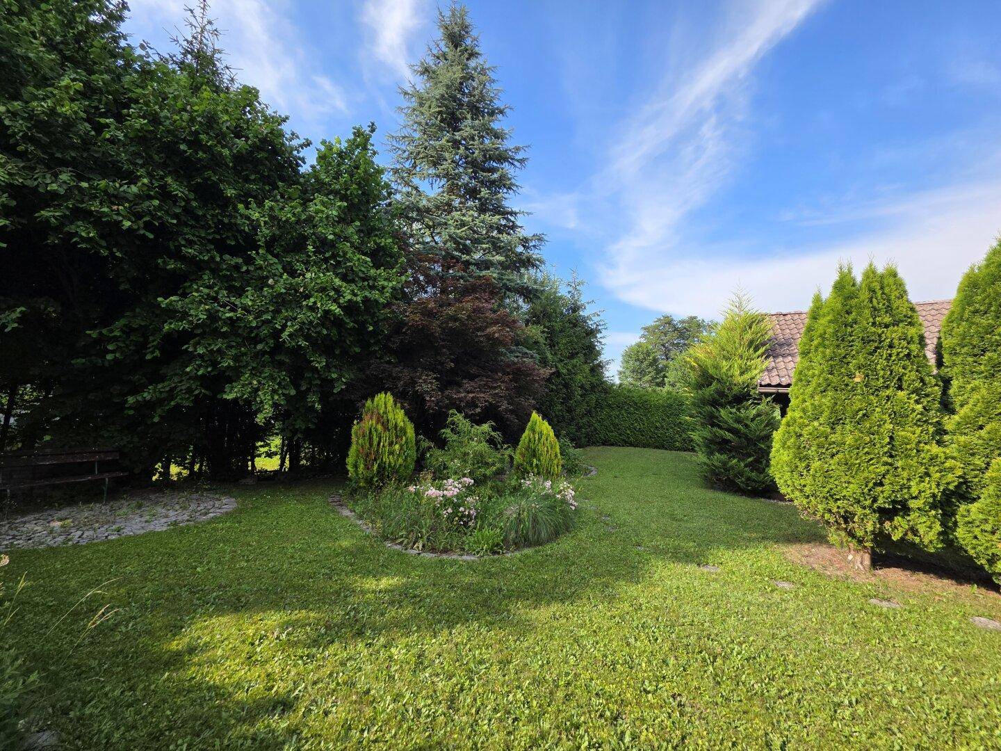 Weitläufiger, gepflegter Garten mit großer Rasenfläche und vielfältigem Baumbestand unter strahlend blauem Himmel.