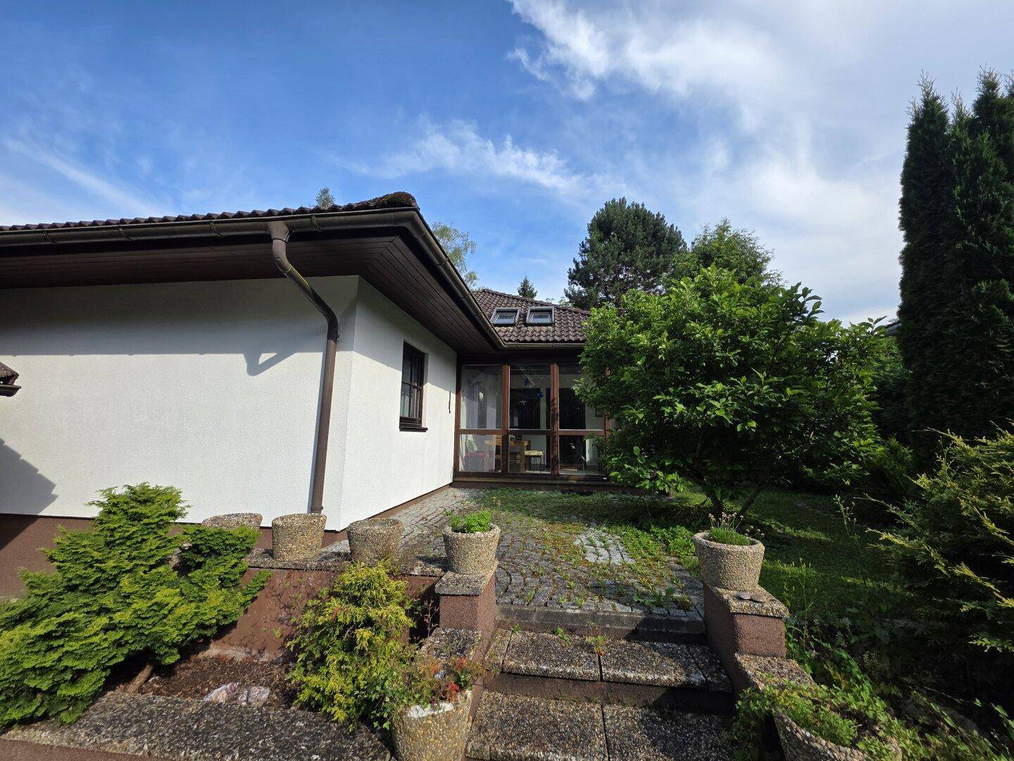 Seitenansicht des Hauses mit weißer Fassade, braunem Dach und Zugang zum Gartenbereich über eine kleine Treppe.