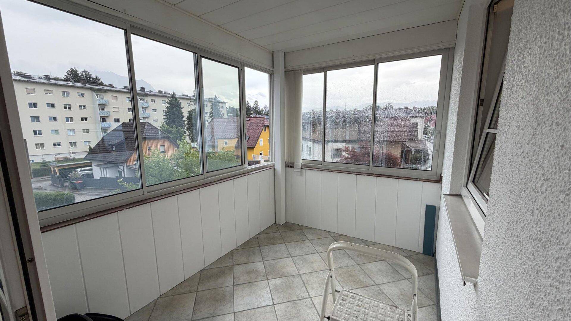 Verglaste Loggia mit Fliesenboden und weitem Blick auf die umliegenden Gebäude und Berge.