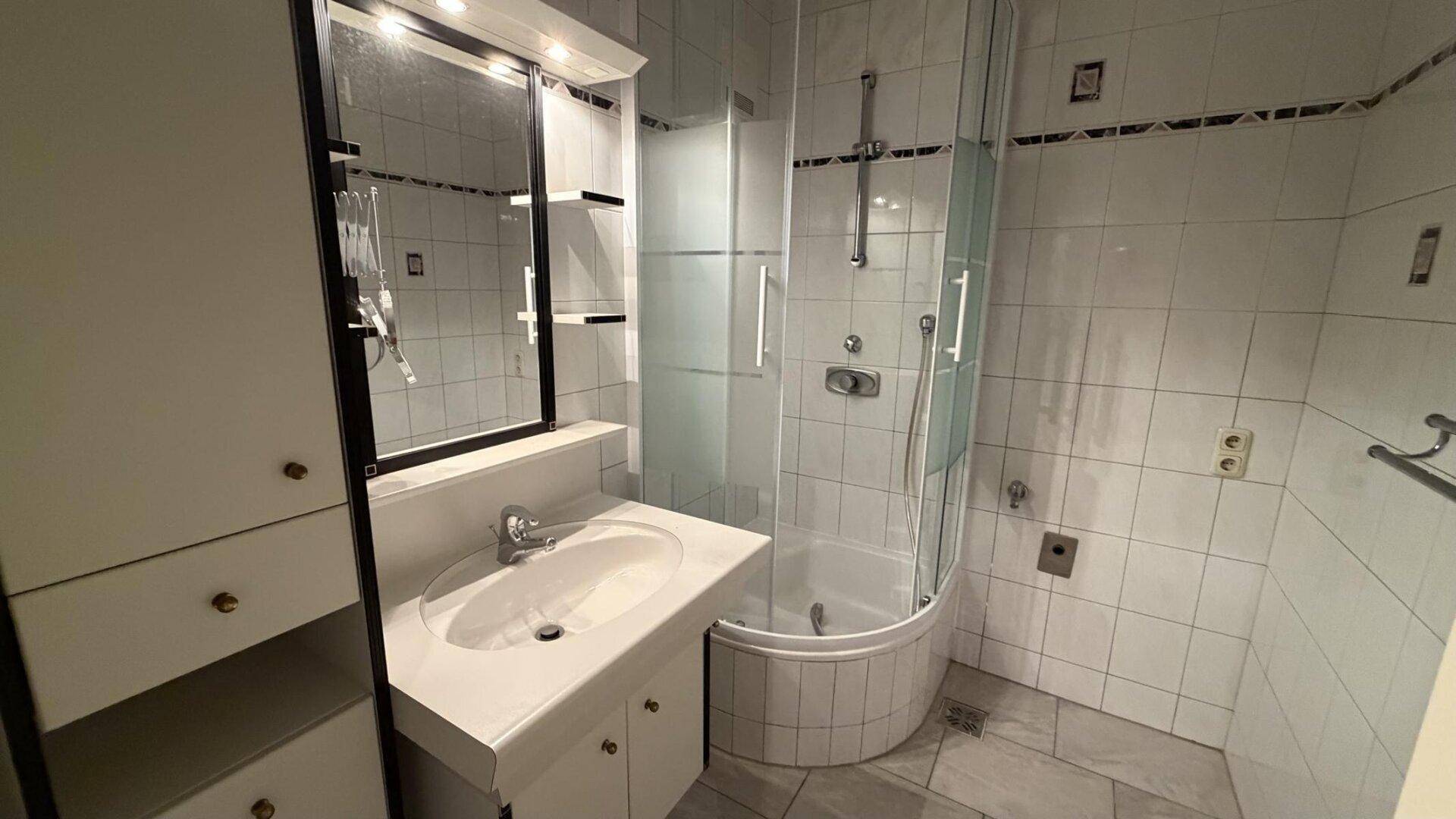 Badezimmer mit Duschkabine, Waschtisch und Spiegelschrank, vollständig gefliest.