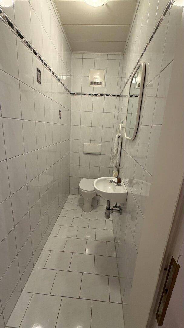 Kleines Gäste-WC, komplett gefliest mit Toilette und Handwaschbecken.