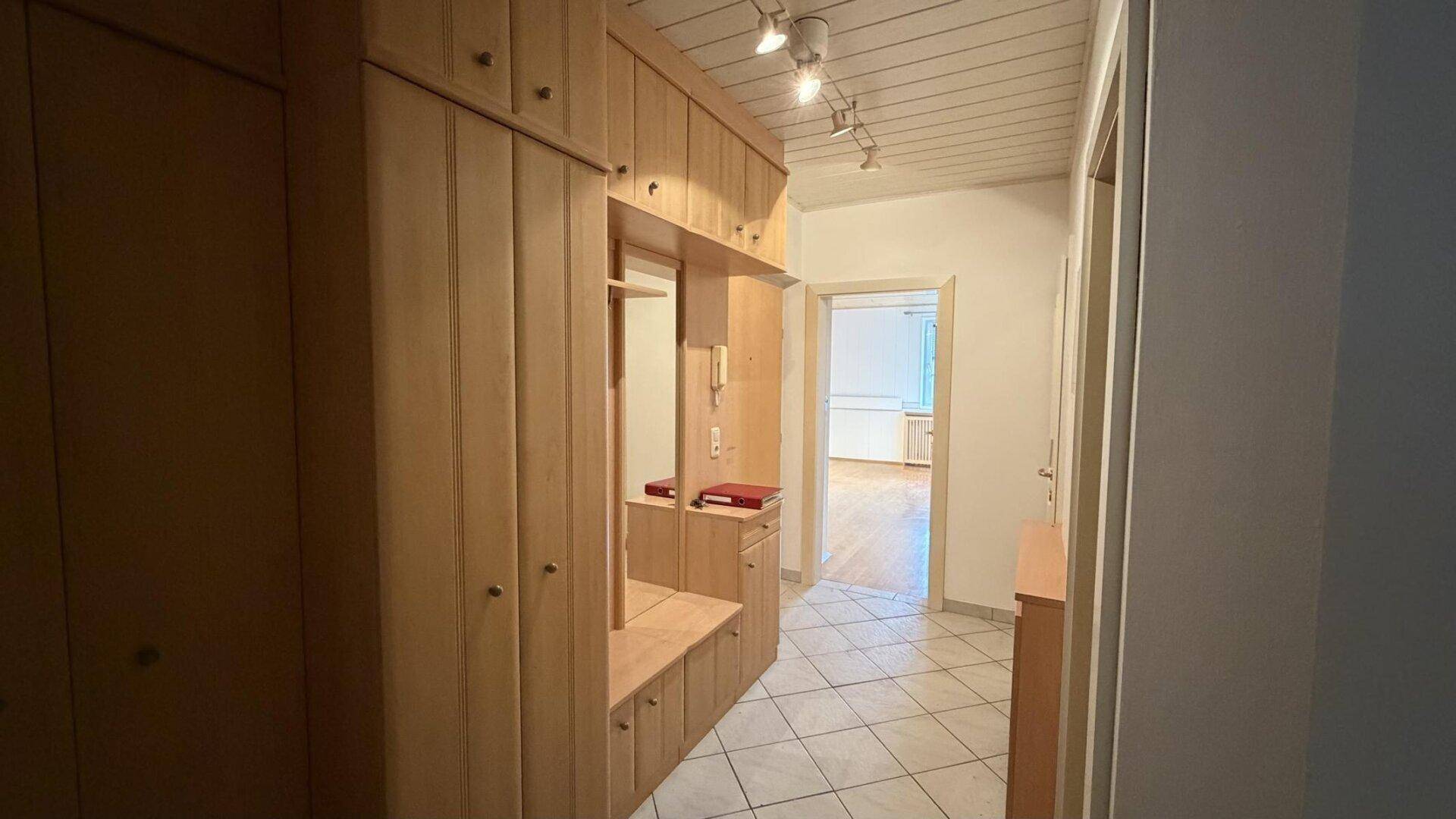 Flur mit integriertem Holzschrank, Fliesenboden und Zugang zu weiteren Räumen.
