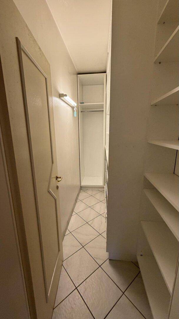 Begehbarer Kleiderschrank mit praktischen Regalen und Fliesenboden.
