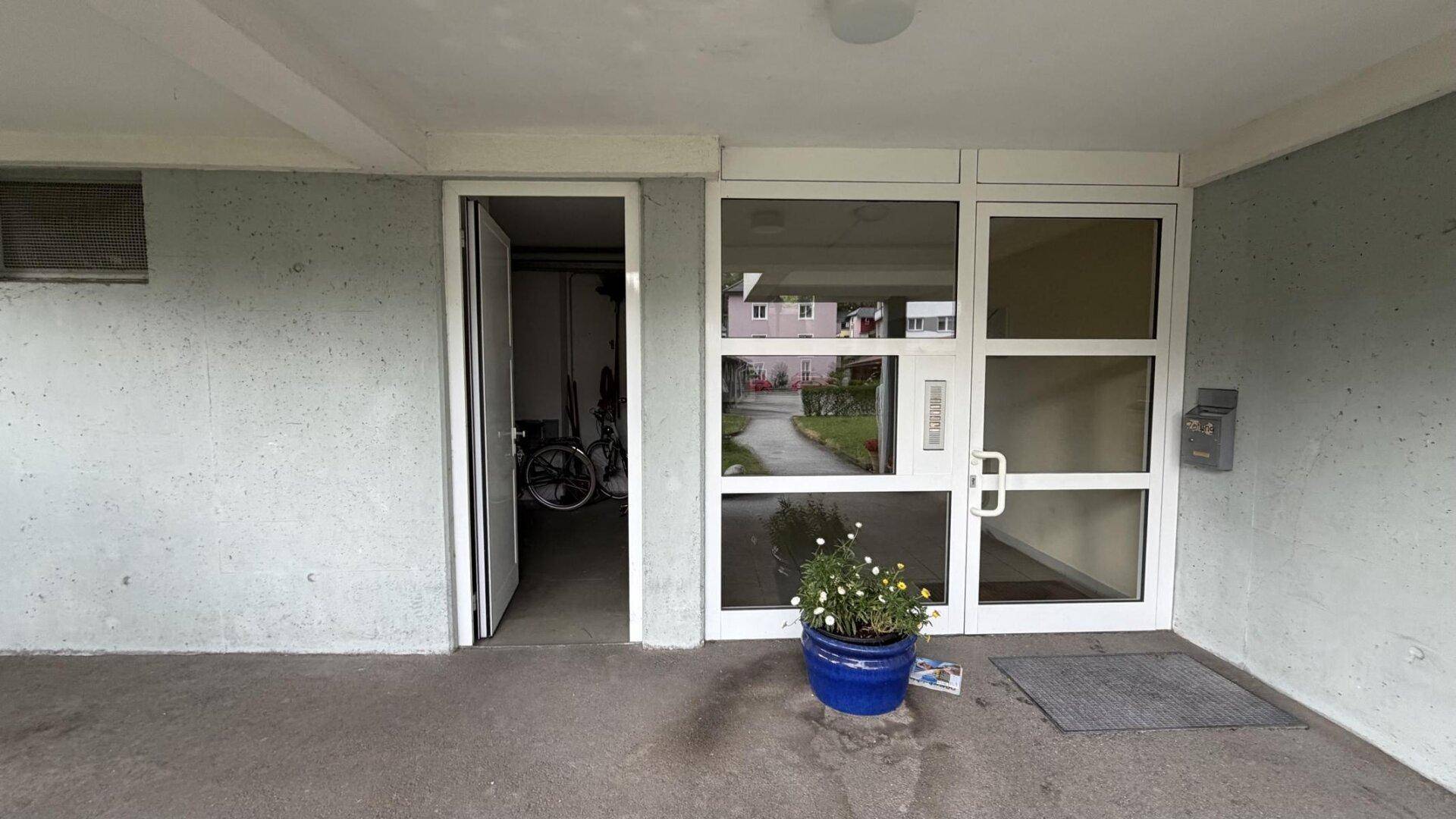 Eingangsbereich des Gebäudes mit großer Glastür und Topfpflanze.
