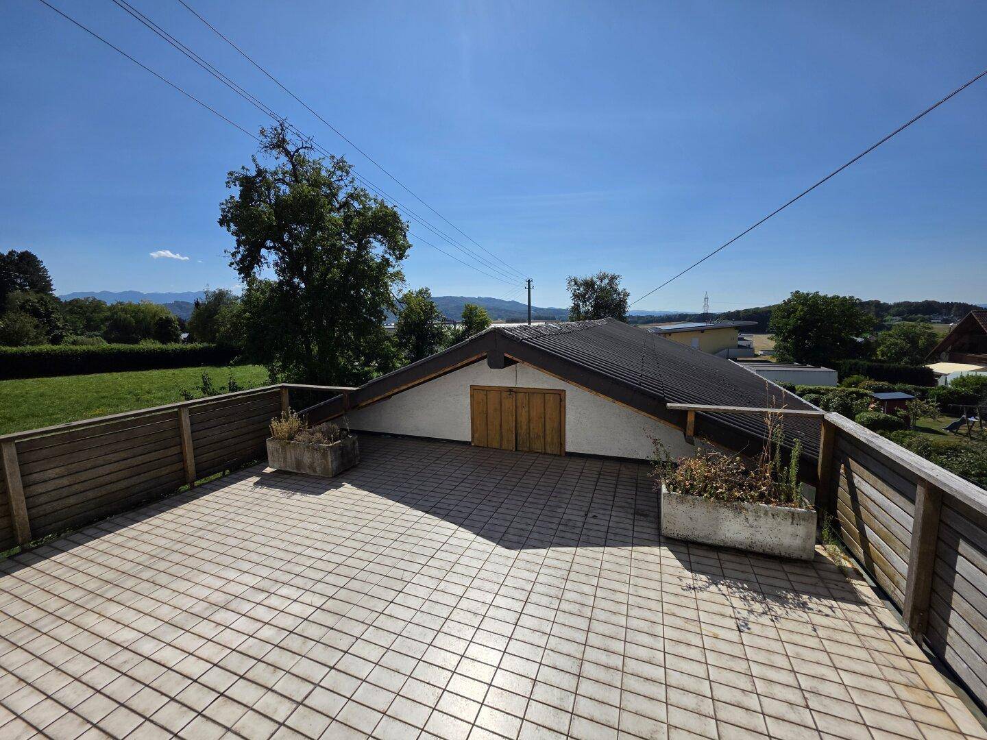 Große geflieste Terrasse mit Holzzaun und weitem Blick auf die Landschaft.