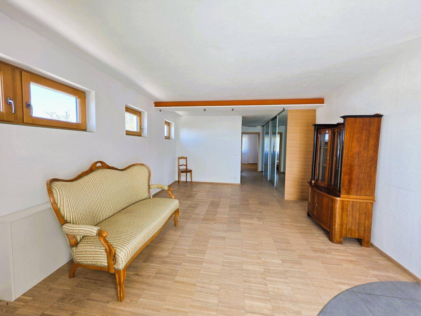 Großzügiges Wohnzimmer mit Parkettboden, klassischem Sofa und viel Tageslicht.