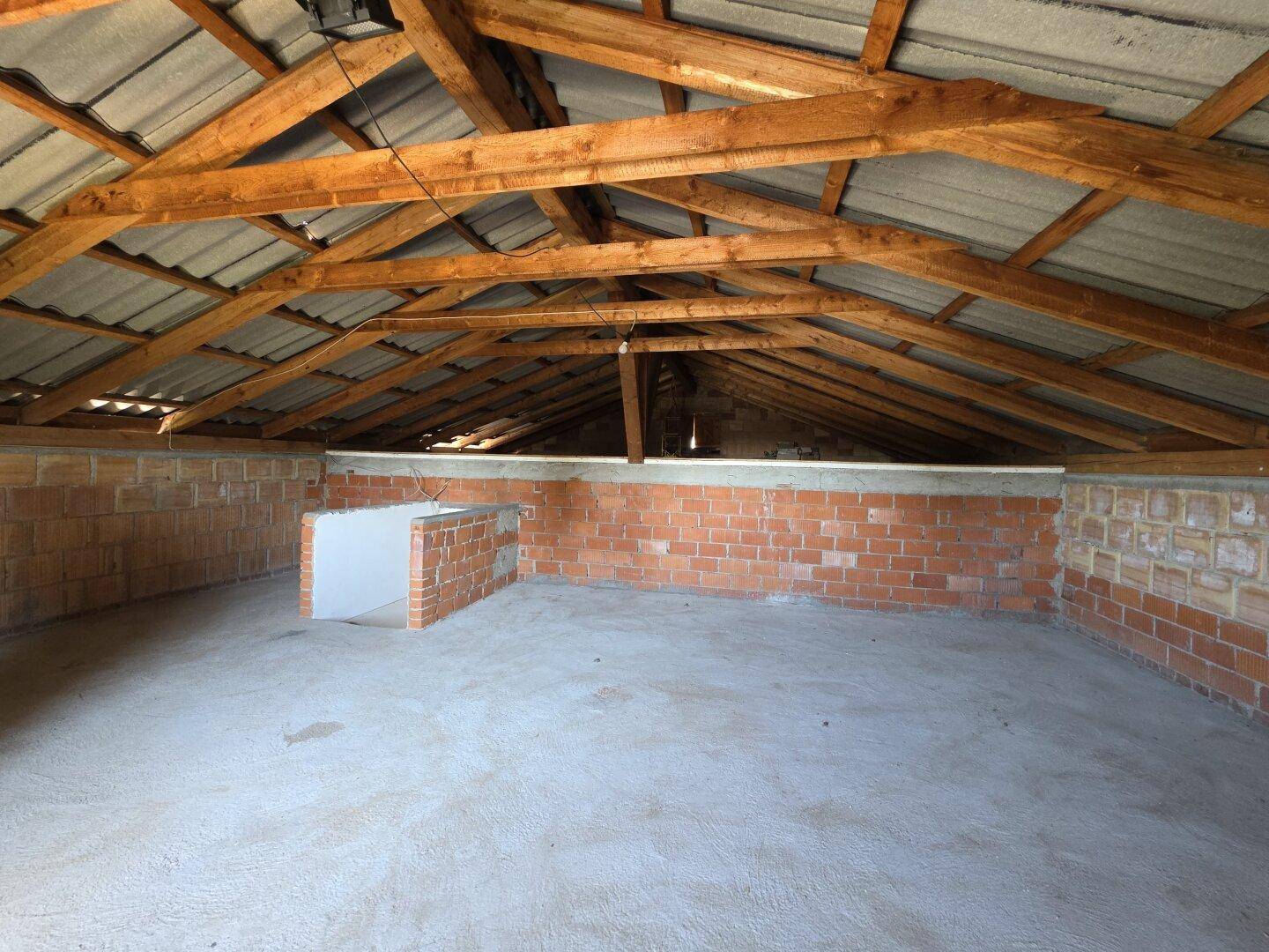 Unausgebauter Dachboden mit sichtbaren Holzbalken und niedrigen Ziegelwänden.