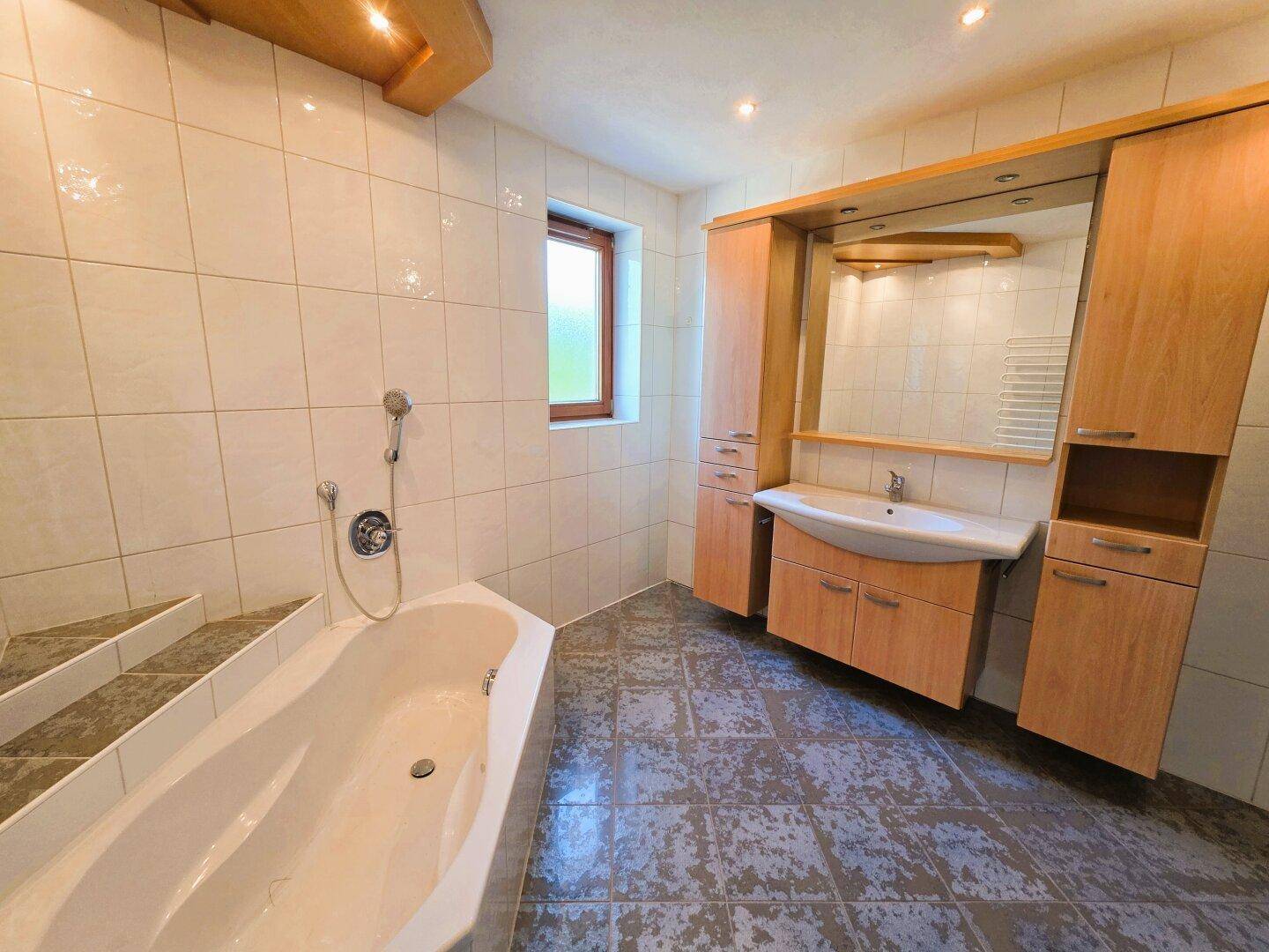 Geräumiges Badezimmer mit Badewanne, Waschtisch und Holzschränken.