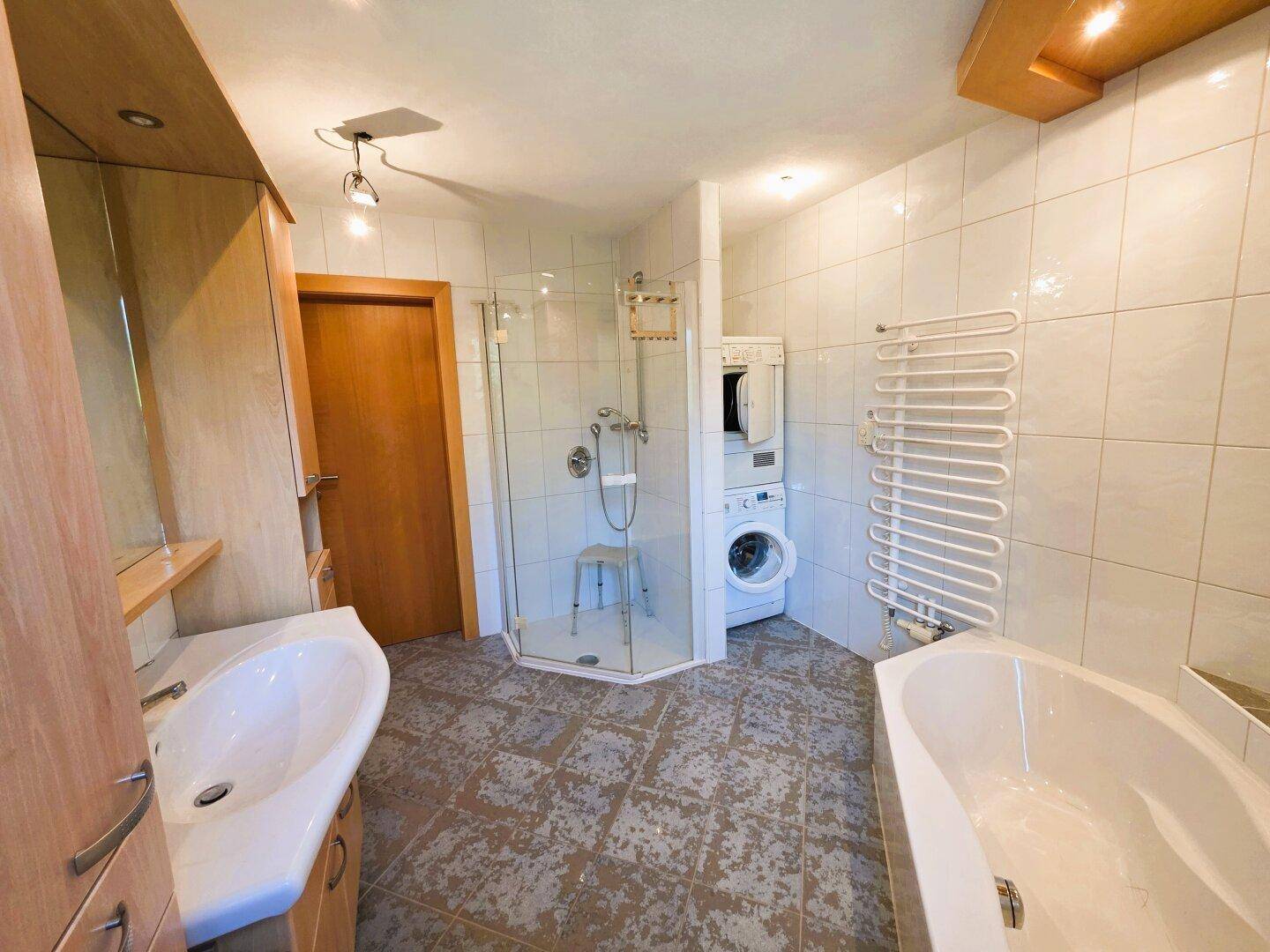 Helles Badezimmer mit Badewanne, Dusche, Waschmaschine und Trockner.