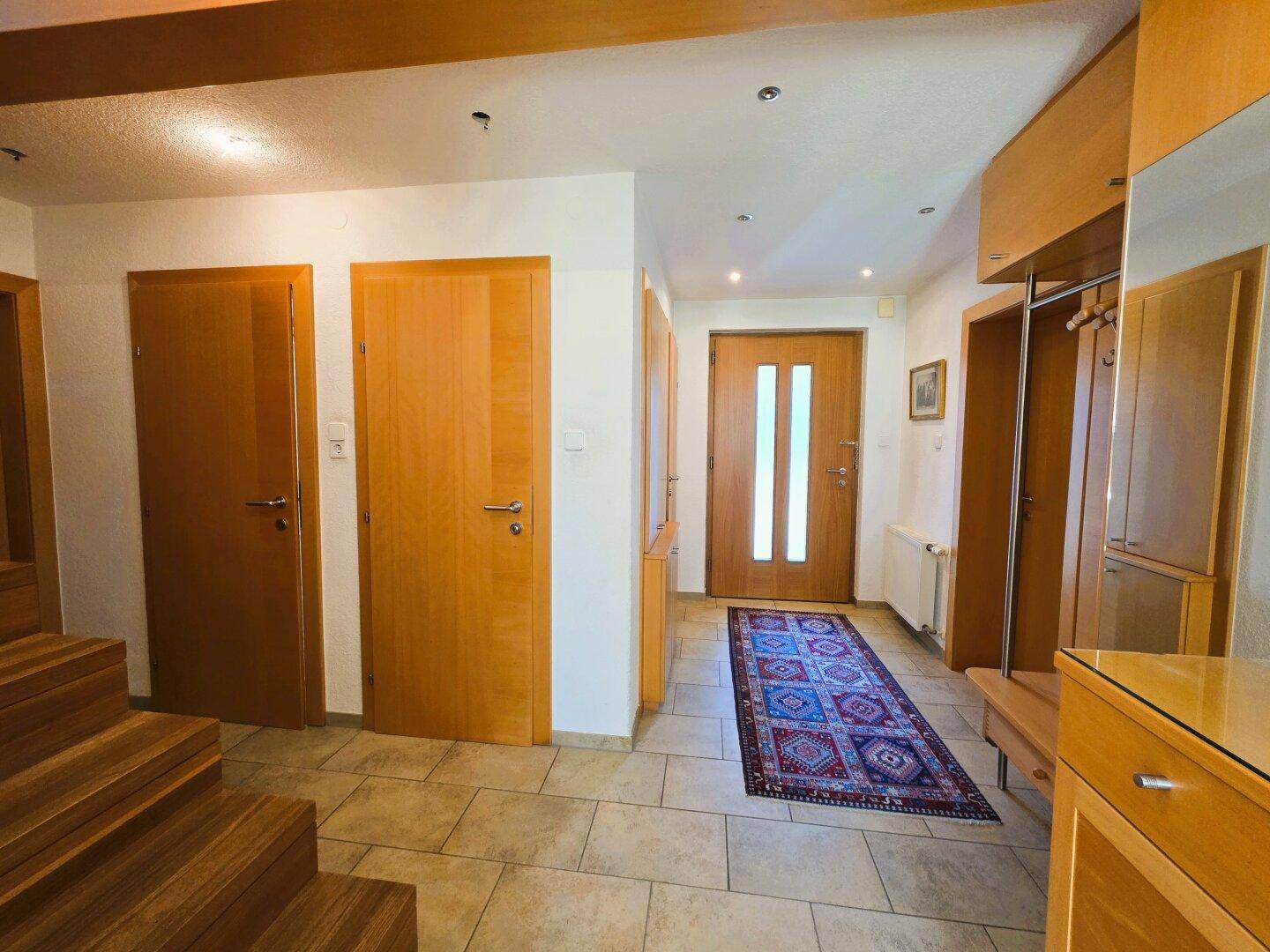 Heller Eingangsbereich mit Fliesenboden, Holztreppe und Garderobe.