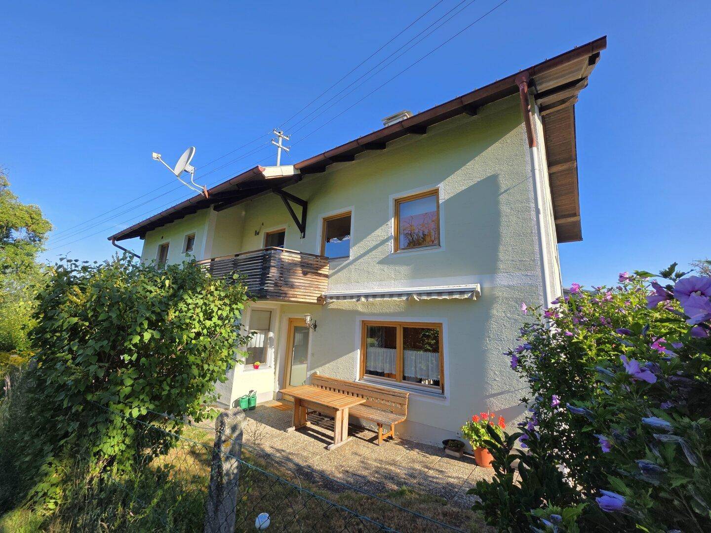 Einfamilienhaus mit Balkon, Terrasse und gepflegtem Garten unter blauem Himmel.