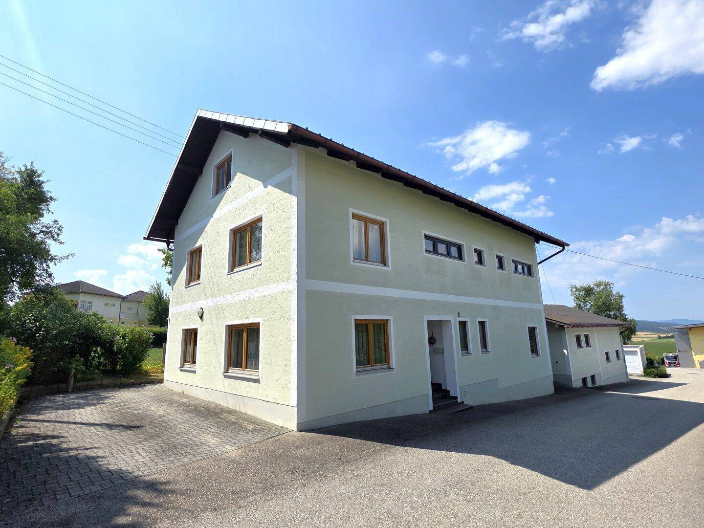 Ansicht des Wohnhauses mit hellgrüner Fassade, braunen Fenstern und gepflasterter Einfahrt.
