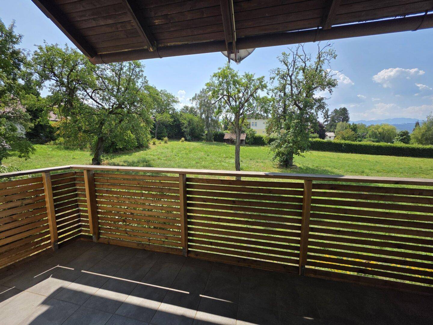 Großer Holzbalkon mit weitem Blick auf die grüne Landschaft und Berge.