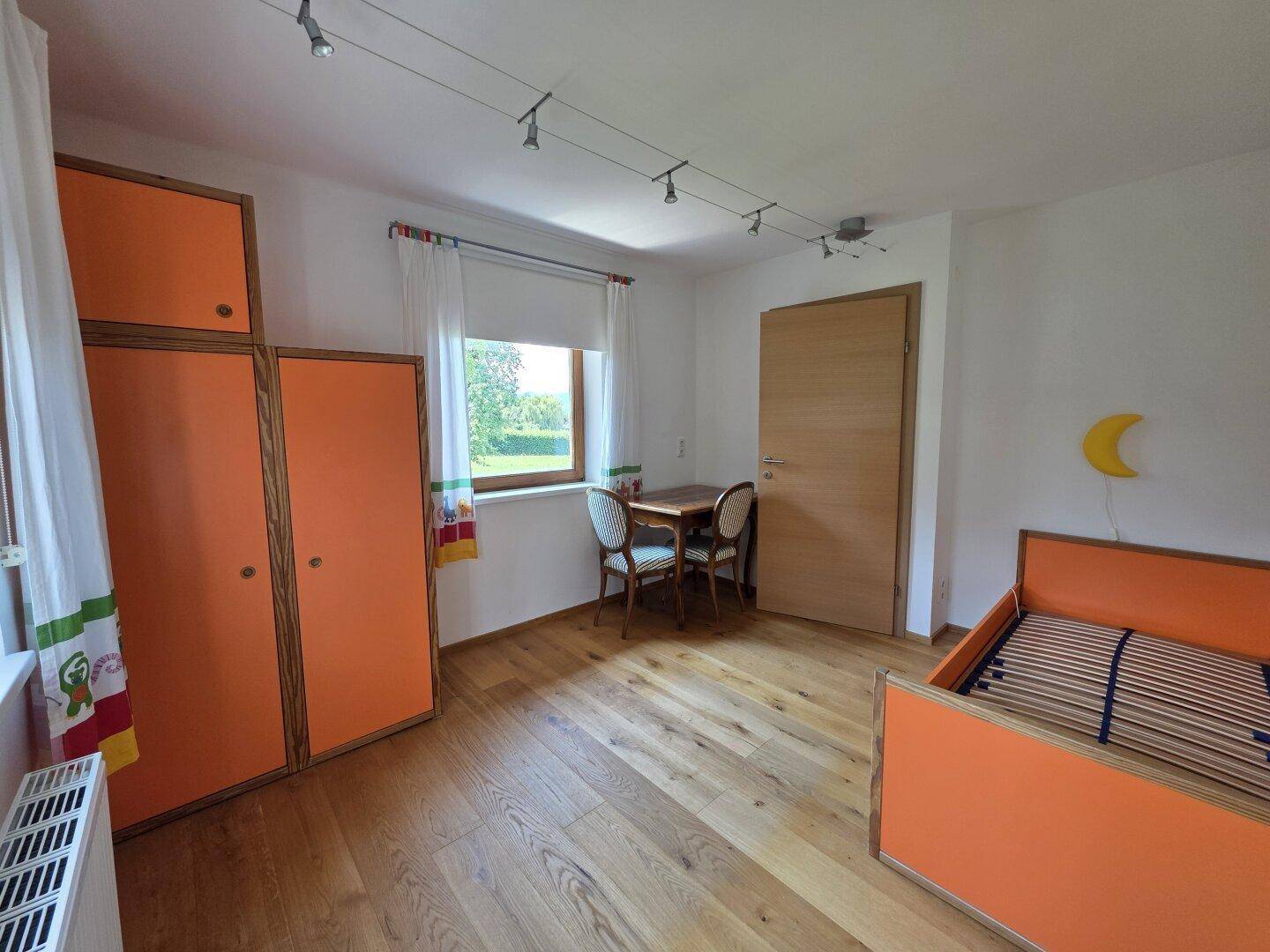Helles Kinderzimmer mit orangefarbenen Schränken, Holzboden und Schreibtisch.