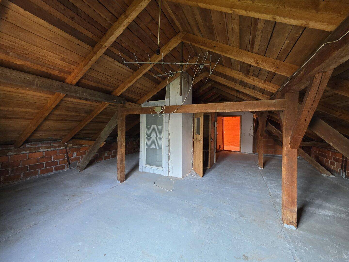 Unausgebauter Dachboden mit sichtbaren Holzbalken und Ziegelwänden, bereit für den Ausbau.