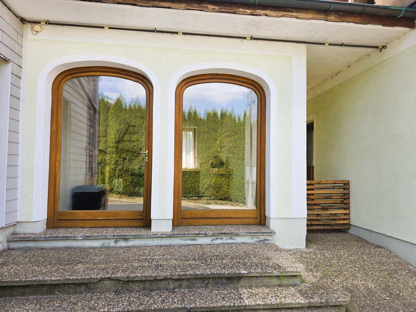 Zwei große, gewölbte Glastüren mit Holzrahmen am Eingang des Gebäudes.
