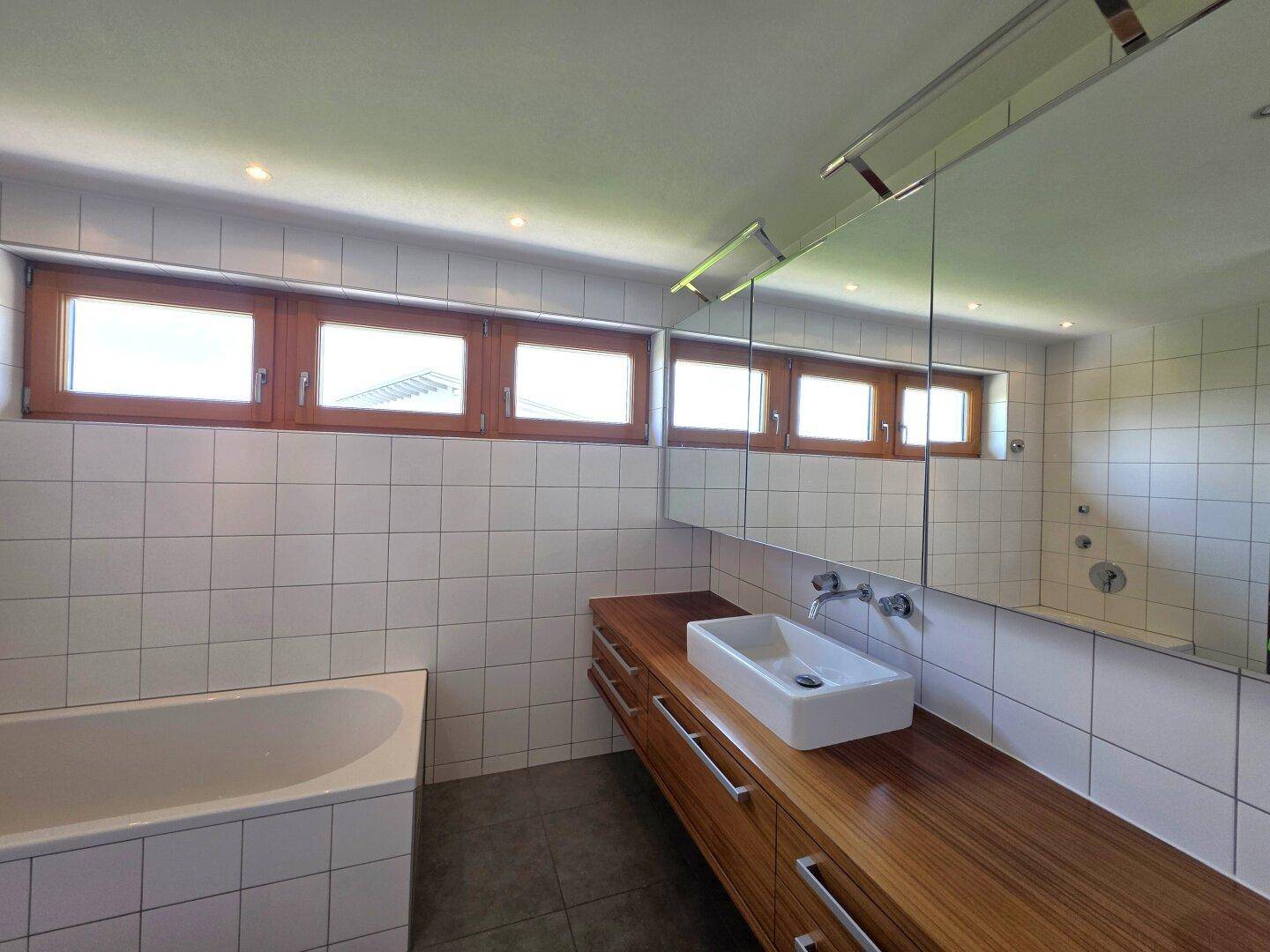 Modernes Badezimmer mit Badewanne, Holzwaschtisch und vielen Fenstern.