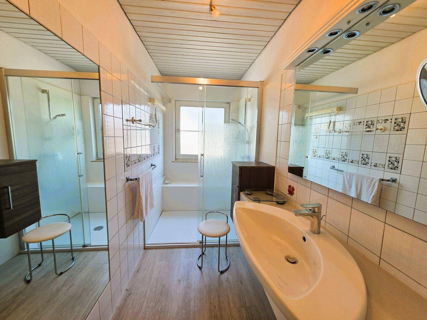 Helles Badezimmer mit Dusche, großem Spiegel und Holzdeckenverkleidung, bietet viel Tageslicht.