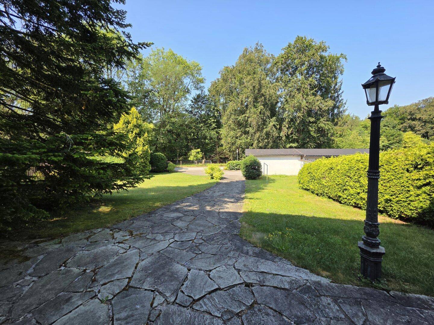 Gepflegter Garten mit altem Laternenpfahl, Bäumen und einem malerischen Steinweg.