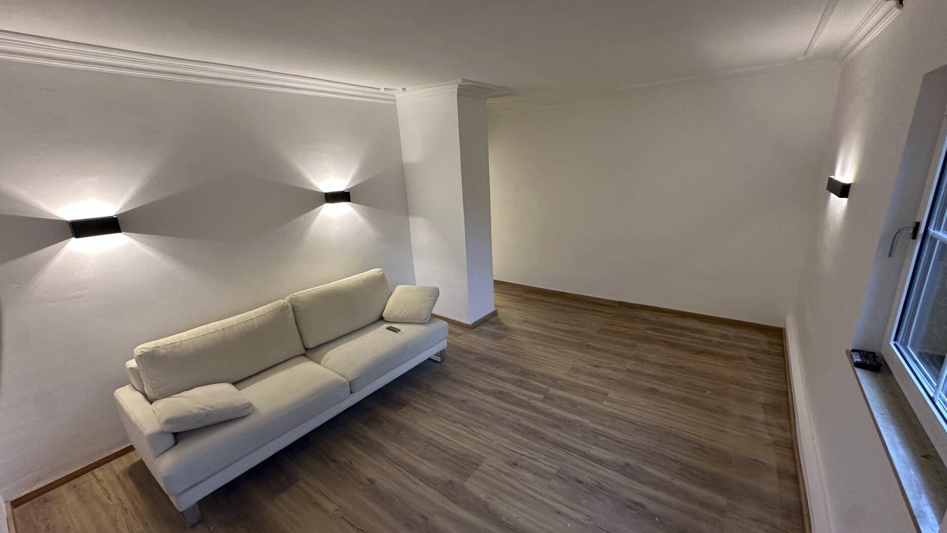 Gemütliches Wohnzimmer mit indirekter Beleuchtung und hellem Laminatboden, schafft eine warme Atmosphäre.