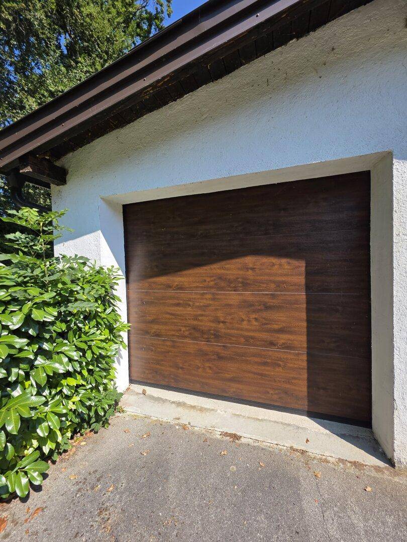 Einzelgarage mit modernem Holz-Garagentor und umgebendem grünen Bewuchs.
