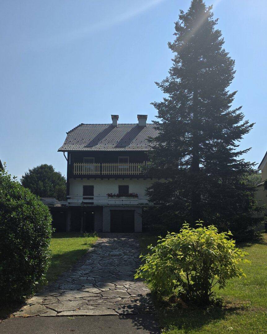 Traditionelles Haus mit Balkonen, Satteldach und großem Nadelbaum im Vorgarten.