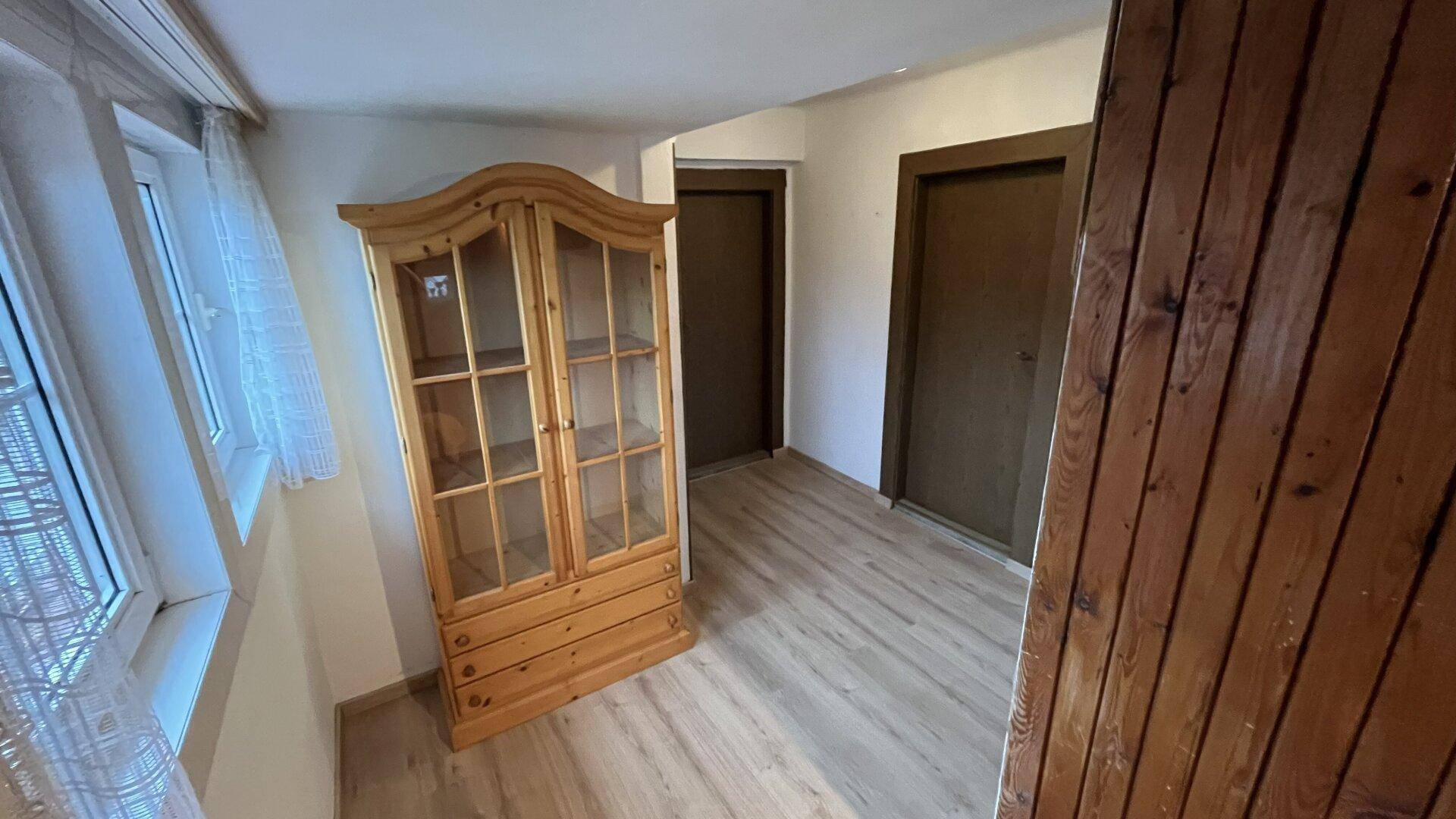 Flur mit Holzschrank, Laminatboden und Zugang zu weiteren hellen Räumen.