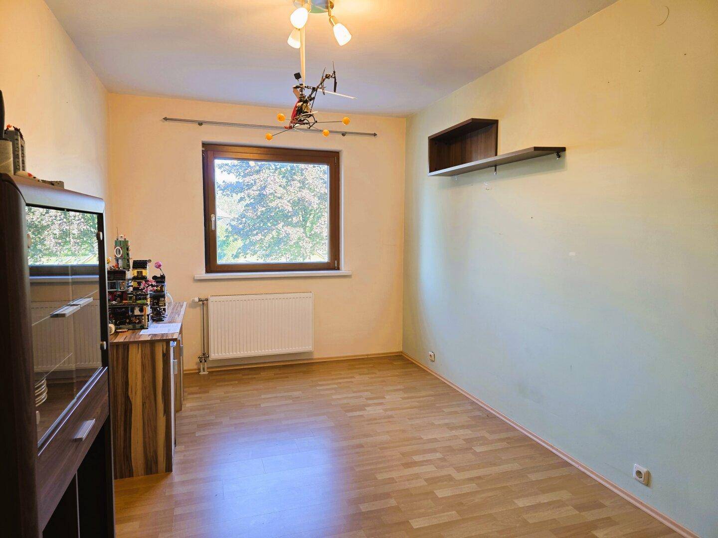 Gemütliches Schlafzimmer mit Laminatboden, Fenster und Blick ins Grüne, ideal für Ruhe und Entspannung.