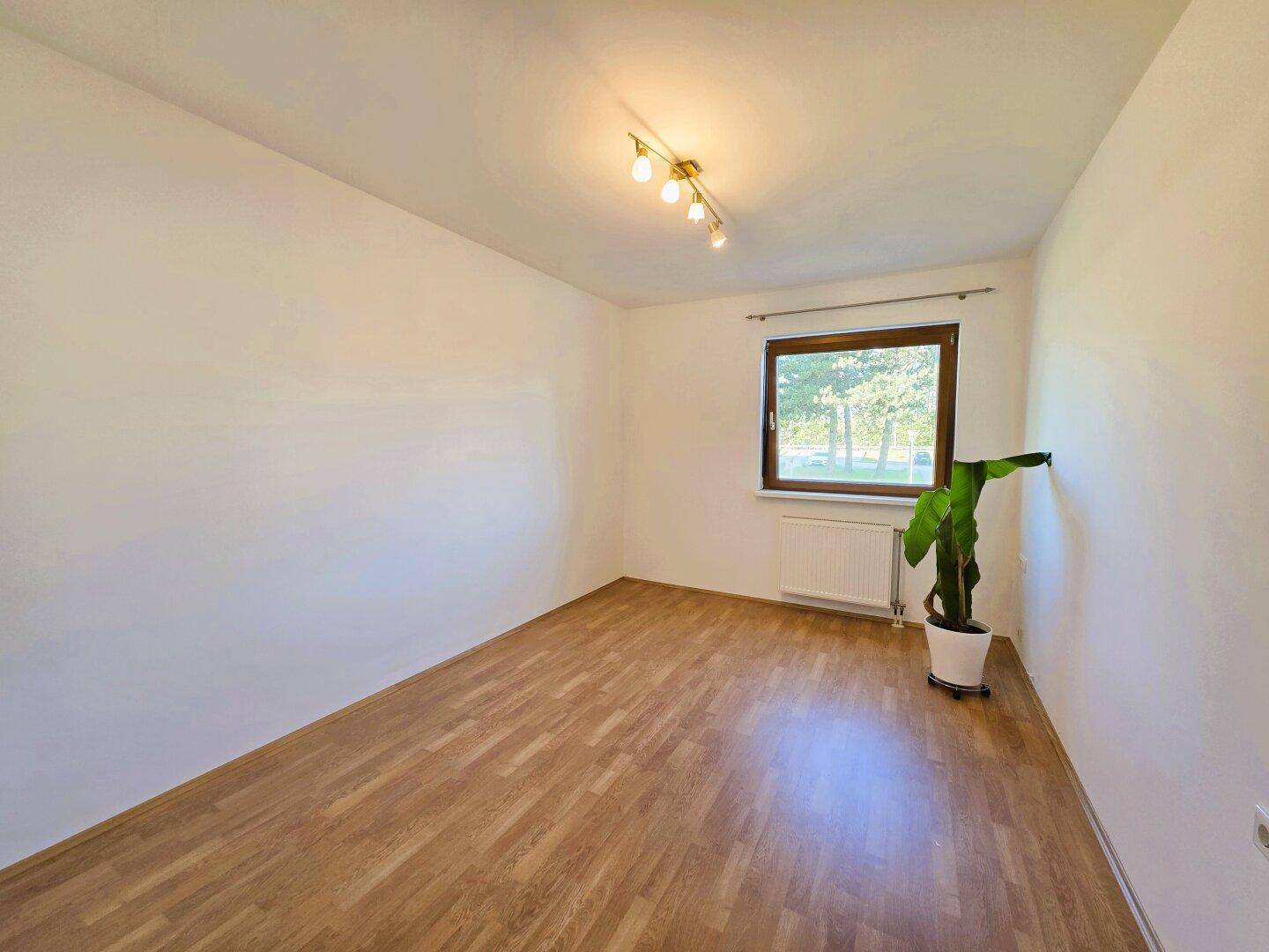 Helles Schlafzimmer mit Laminatboden und großem Fenster, bietet viel Tageslicht und eine angenehme Atmosphäre.