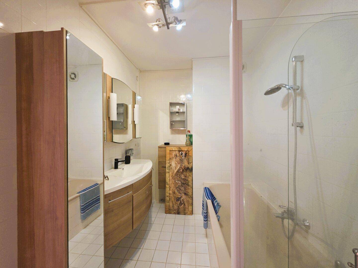 Modernes Badezimmer mit Dusche, Waschbecken und Spiegelschrank, ausgestattet mit hellen Fliesen.