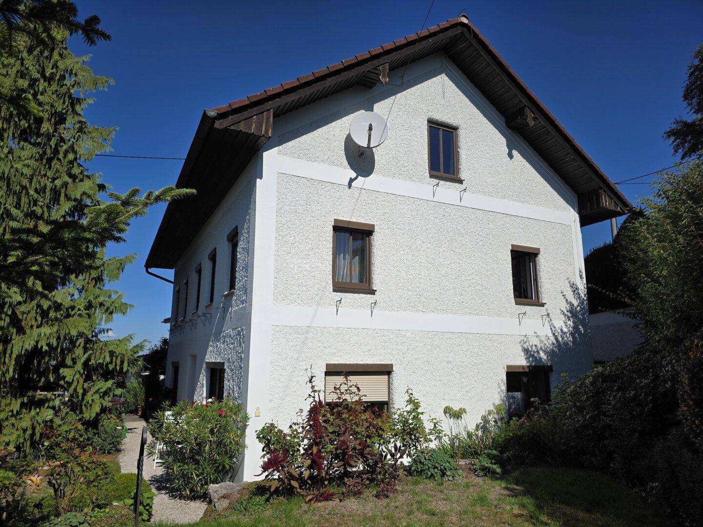 Ansicht des Hauses von der Seite mit gepflegtem Vorgarten und üppiger Bepflanzung unter strahlendem Himmel.