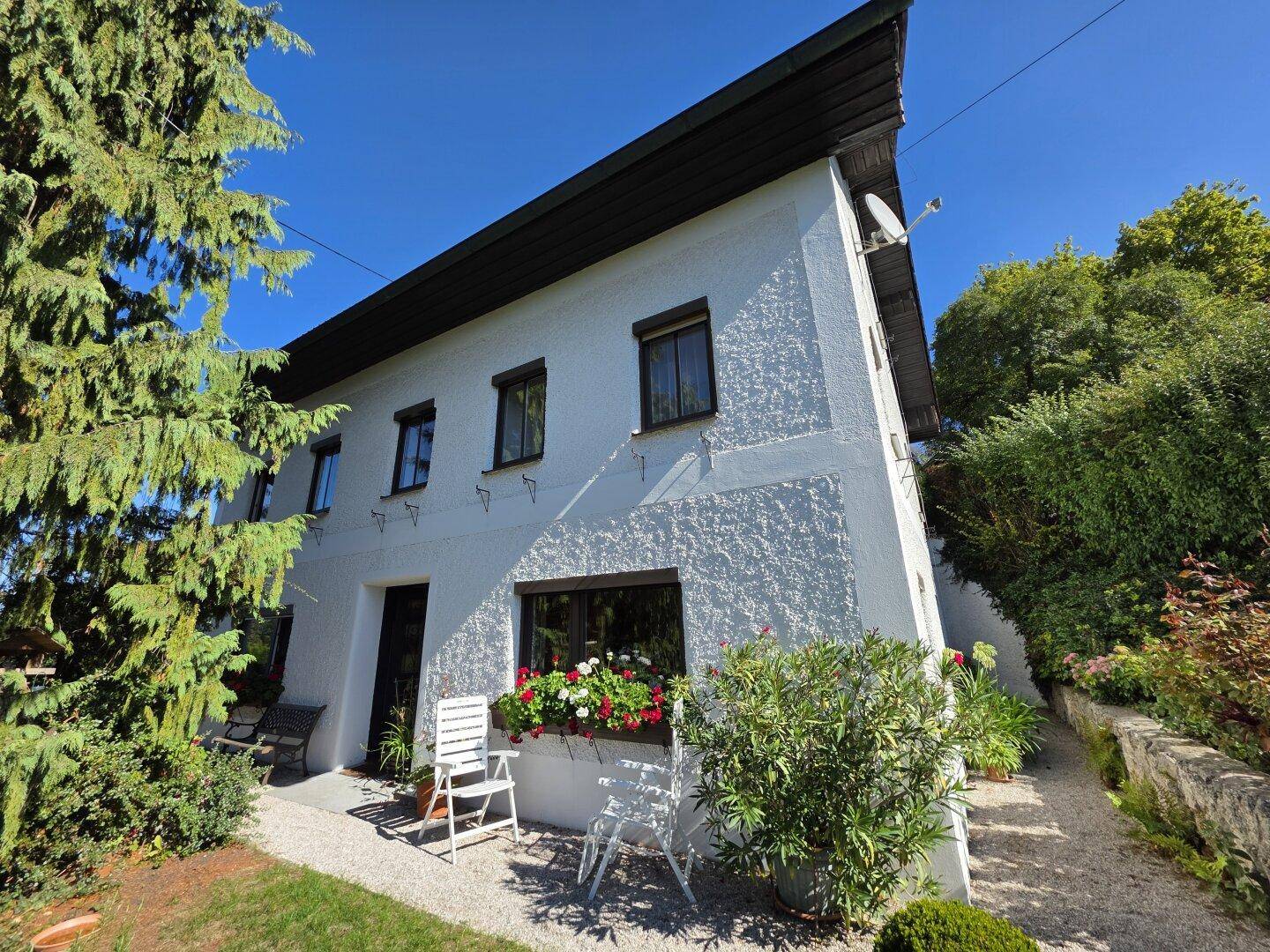 Vorderansicht des Hauses mit blühenden Blumenkästen und einem kleinen, einladenden Sitzbereich im Freien.