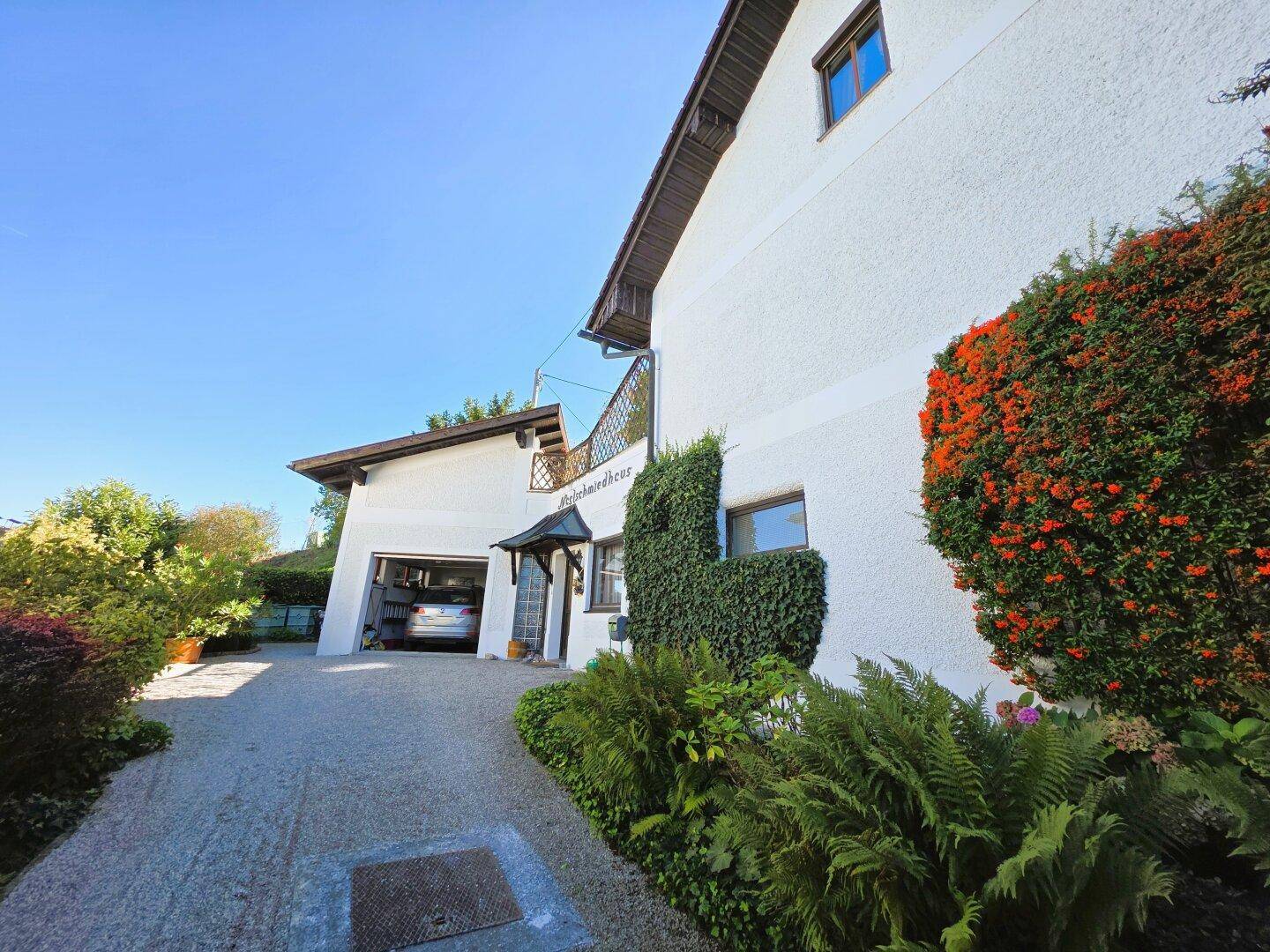 Seitenansicht des Hauses mit Kiesauffahrt zur Garage und üppiger grüner Bepflanzung an der Fassade.