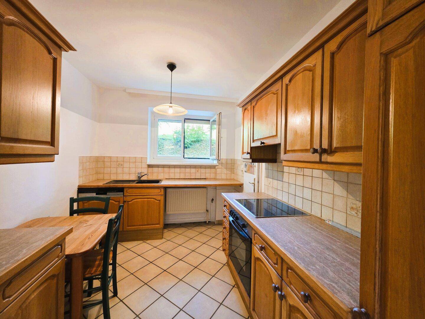 Traditionelle Küche mit Holzschränken, gefliestem Boden und einem Fenster, ausgestattet mit Kochfeld und Spüle.