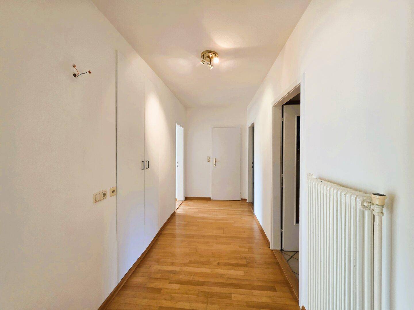 Langer Flur mit Parkettboden, weißen Wänden und praktischen Einbauschränken für zusätzlichen Stauraum.