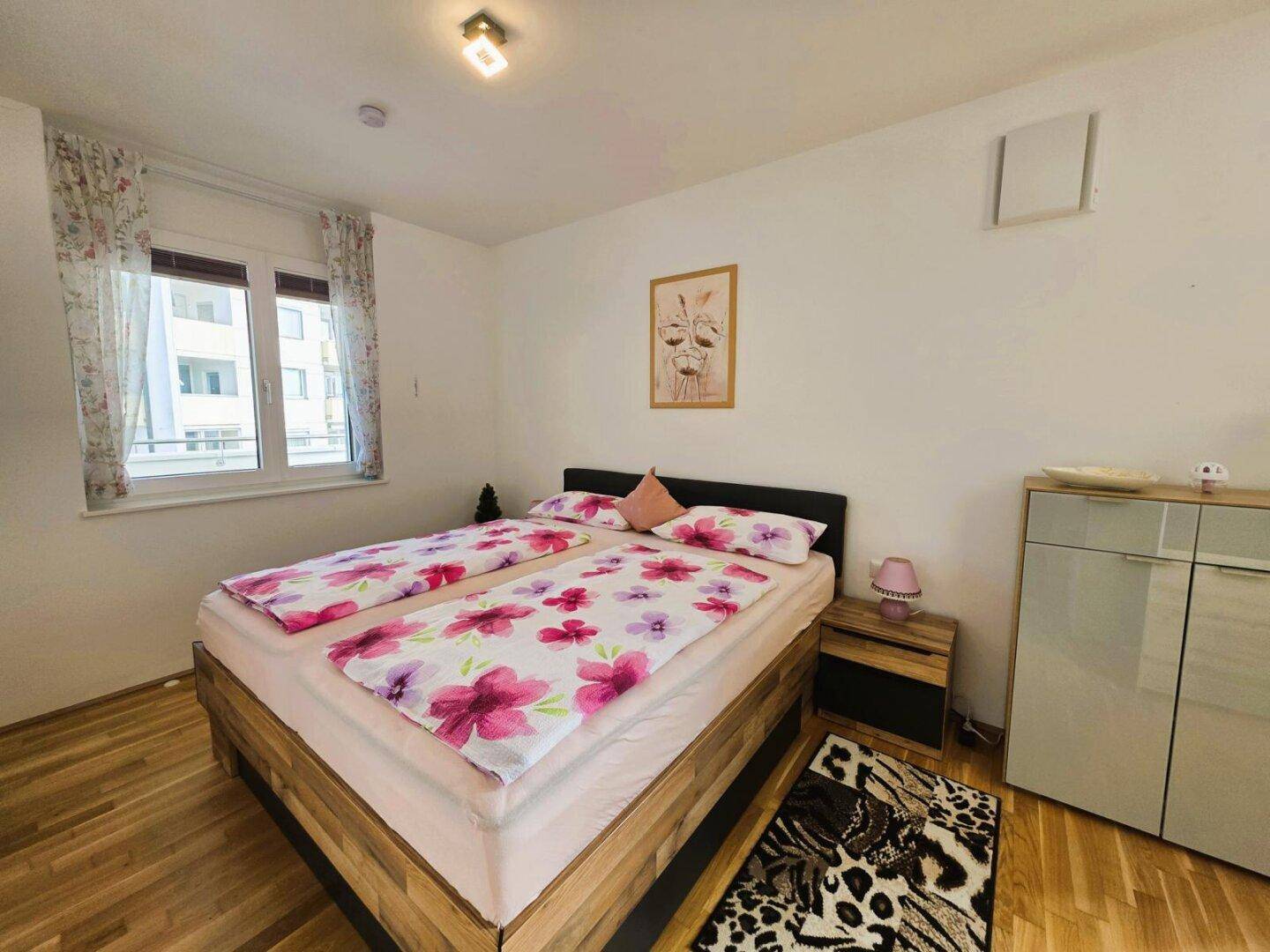 Helles Schlafzimmer mit Doppelbett, Holzboden und Fenster mit Blick nach draußen.